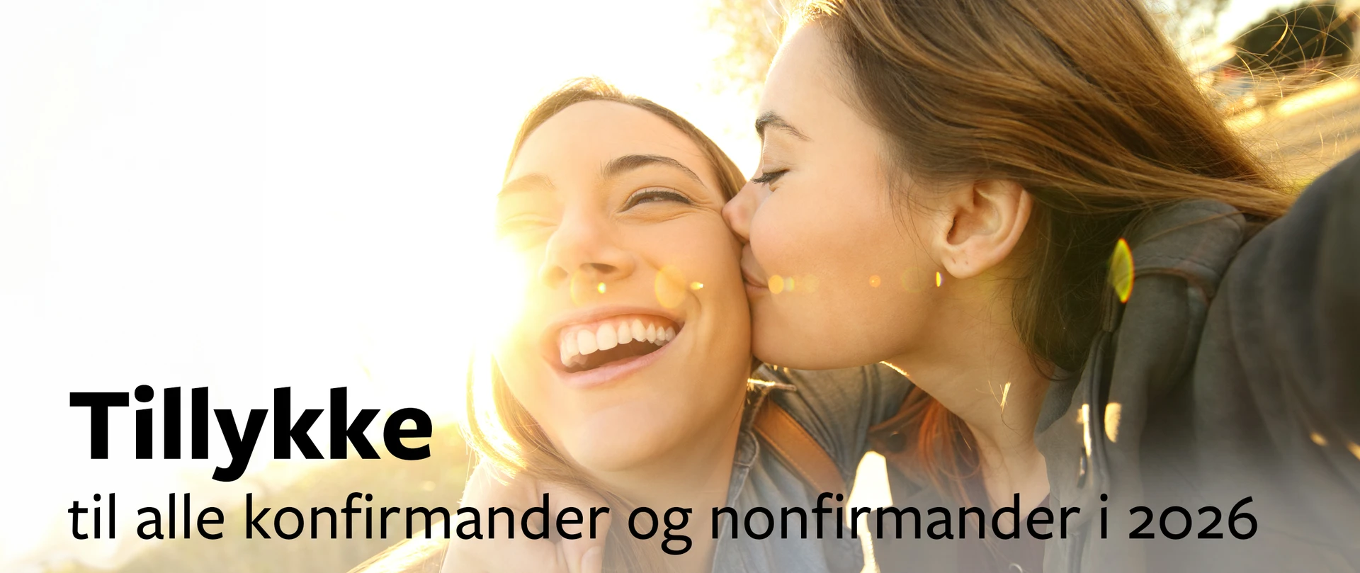 To unge piger hvoraf den ene smiler, imens den anden kysser hende på kinden med teksten: "Tillykke til alle konfirmander og nonfirmander i 2024"