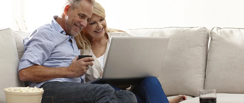 Ældre par i sofa der begge kigger på en laptop