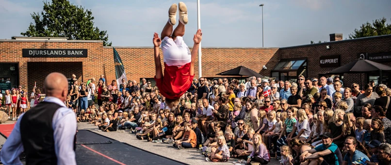 Billede fra jubilæum i Tranbjerg. Flying Superkids junior optræder foran stort publikum. Dreng slår saltomortale i forgrunden.