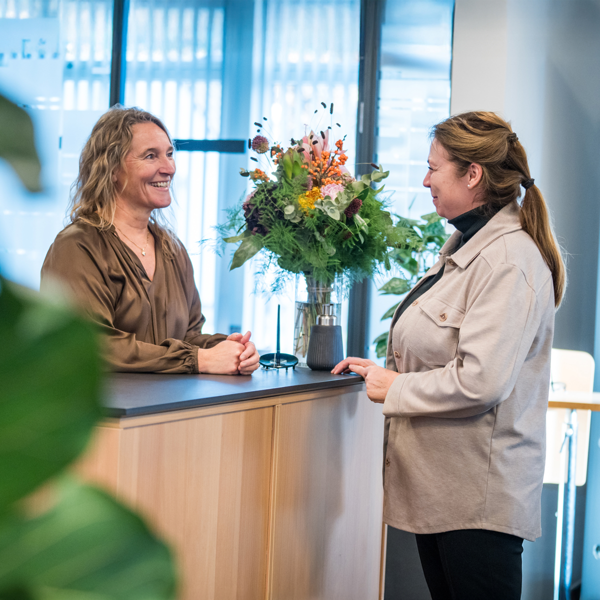 Smilende rådgiver snakker med kunde over et bord, hvorpå der står en stor buket blomster.