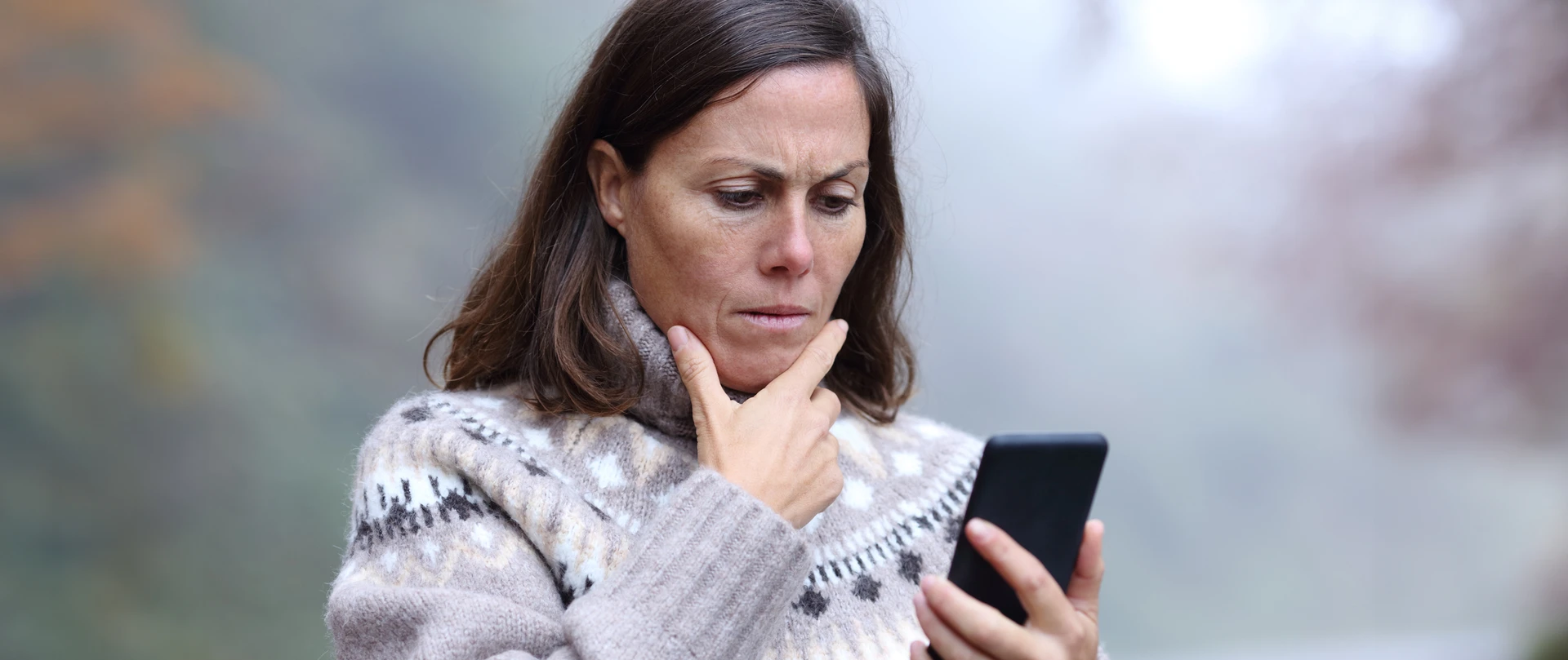 Kvinde står undrende og kigger på sin telefon, imens hun klør sig på hagen.