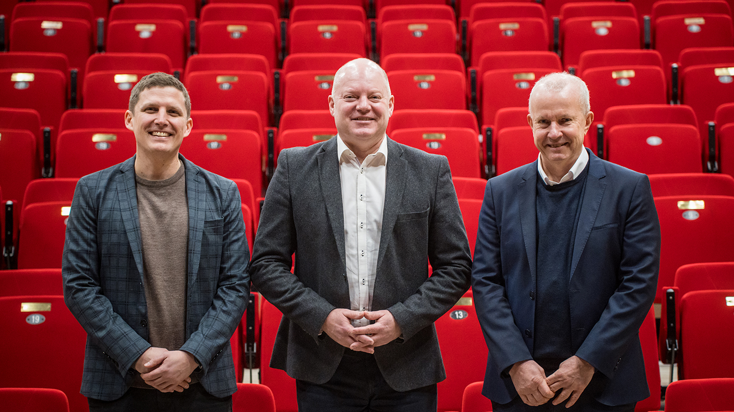 Tre mænd står foran røde biografstole. De tre mænd er områdedirektør Peter Møller, filialdirektør Søren Mandrup Wellejus og Jesper Jul fra Pavillonen. 