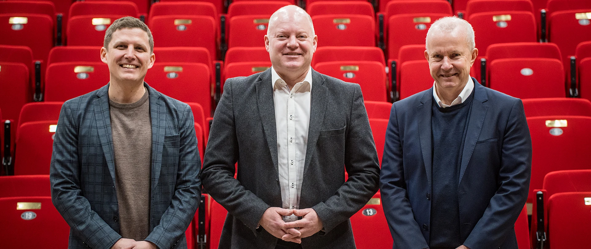 Tre mænd står foran røde biografstole. De tre mænd er områdedirektør Peter Møller, filialdirektør Søren Mandrup Wellejus og Jesper Jul fra Pavillonen.
