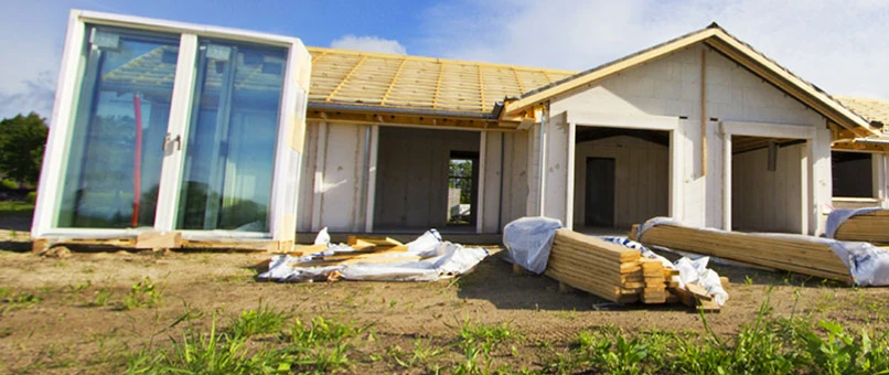 Hus under opførsel. Vinduer og brædder ligger foran huset der endnu ikke har tag eller vinduer.