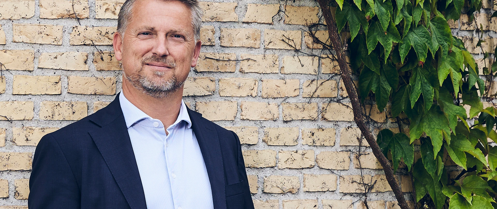 Sigurd Bohlbro Simmelsgaard, Adm. Direktør, CEO i Djurslands Bank foran gul murstensmur.
