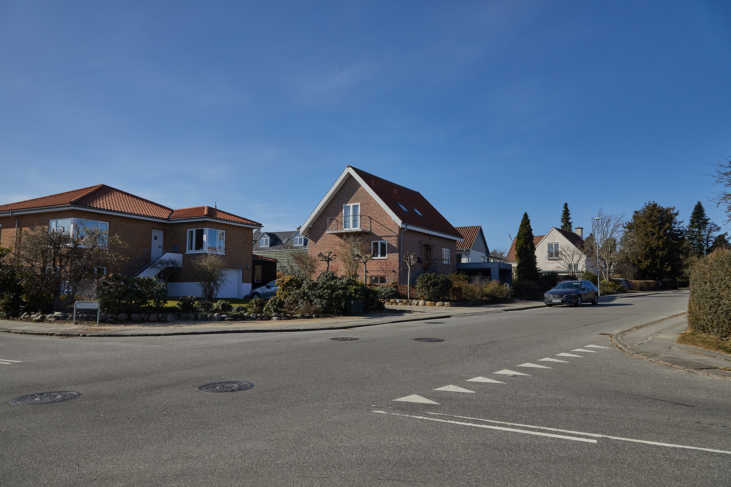 Rødt murstenshus beliggende på en villavej. På vejen foran huset holder en bil parkeret.