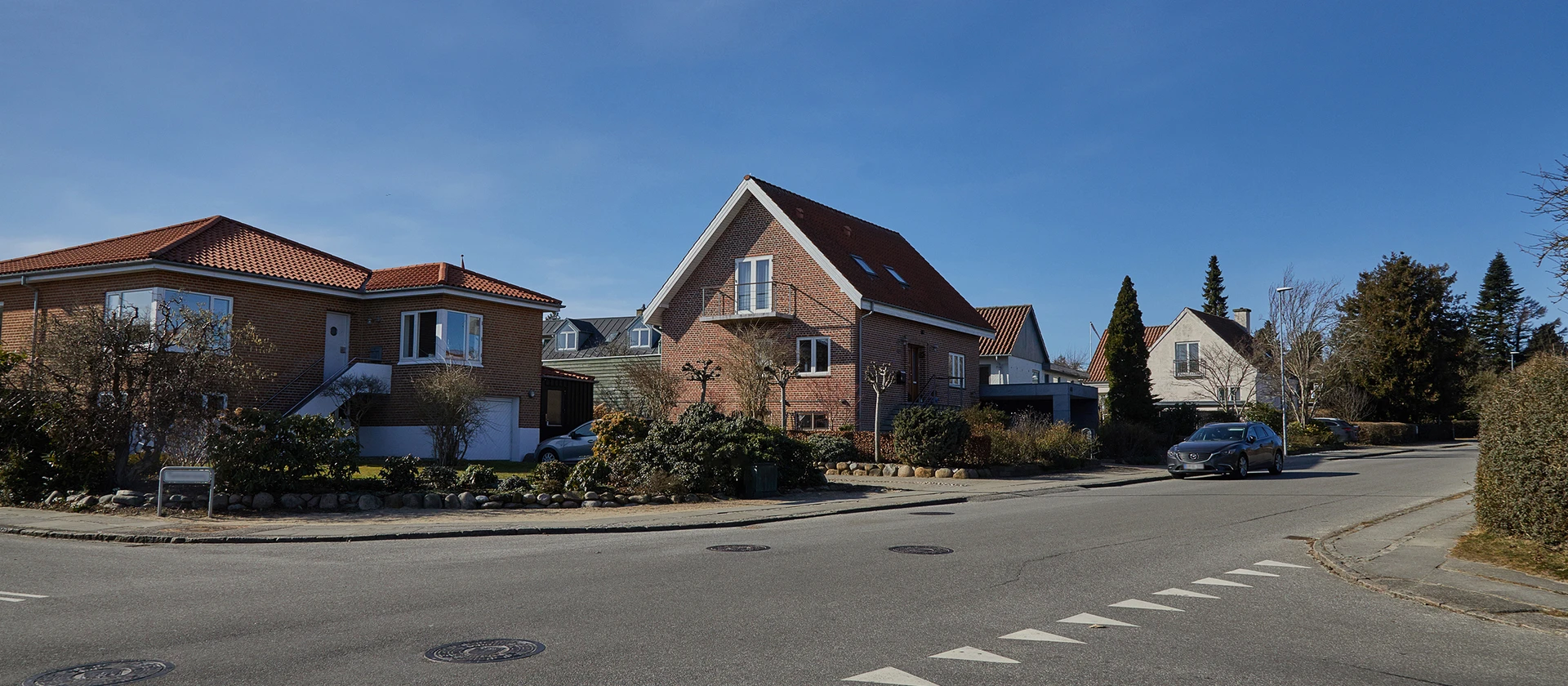 Rødt murstenshus beliggende på en villavej. På vejen foran huset holder en bil parkeret.