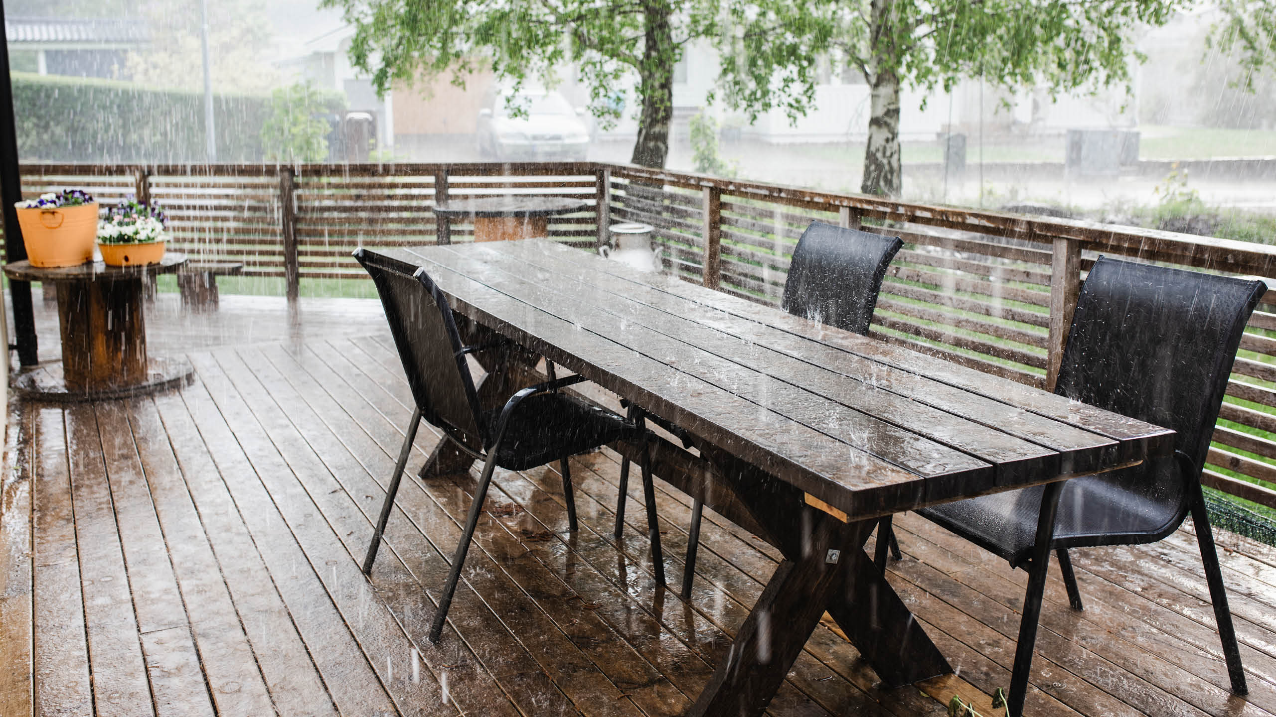 Voldsomt regnvejr på et terrassebord og nogle terrassestole der står på en træterrasse.