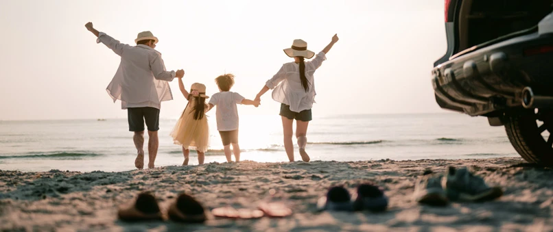 En familie: far, datter, søn og mor, står alle hånd i hånd i vandkanten i solnedgangen. 